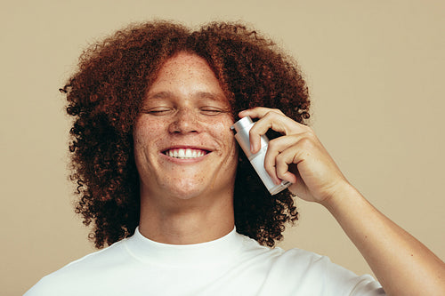 Happy young man applying beauty oil to his face