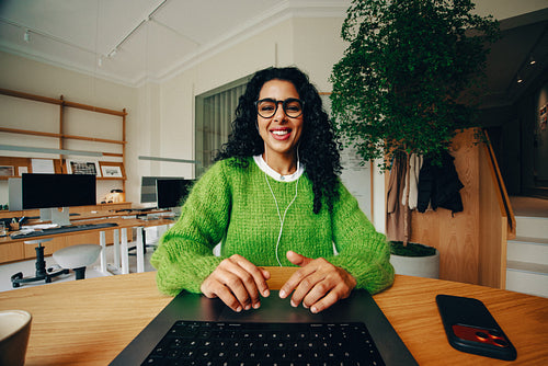 Woman at work in the office smiles while using a laptop and phone at her desk
