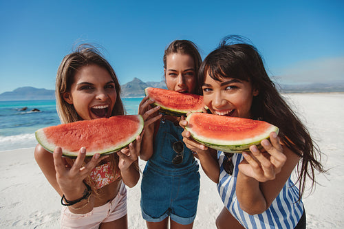 Three young women enjoy fresh watermelon on beach