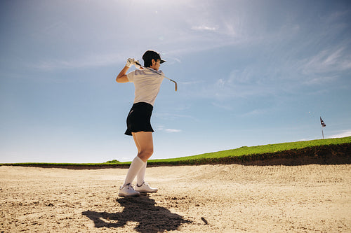 Woman demonstrating hitting golf ball out of sand bunker to putting green