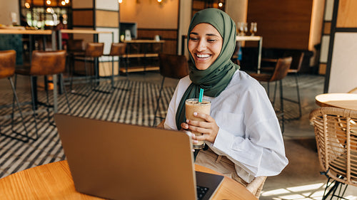 Happy young Muslim woman having a video call in a cafe