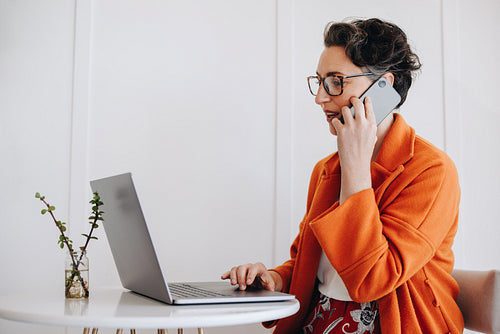 Mature businesswoman speaking on the phone and using a laptop while working in a cafe