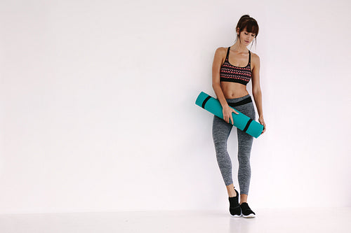 Woman standing with yoga mat in studio