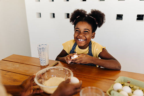 Excited afro-haired girl mixing ingredients for family semolina cake