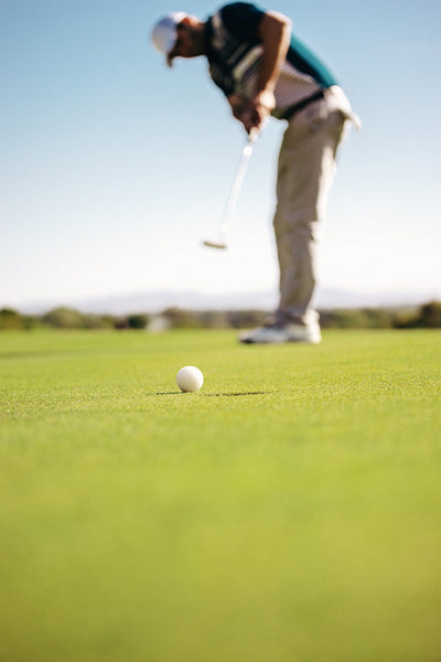 Man swinging club on putting green and focusing on short game during golf practice on sunny day