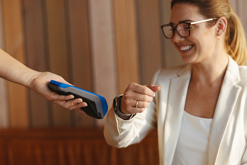 Contactless payment: Working woman paying with with her smartwatch on card reader in a coffee shop