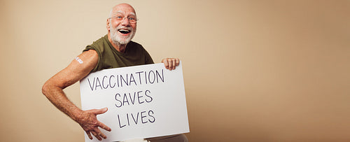 Cheerful senior holding a banner with "vaccination saves lives"