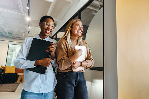 Two female colleagues sharing a laugh at work in an office setting