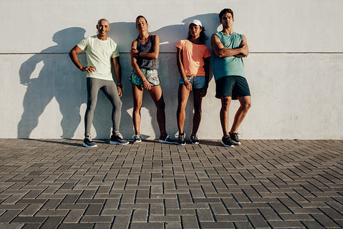 Fitness group posing by a wall outdoors