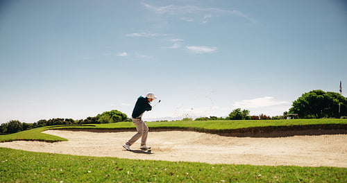 Sportsman swinging golf club for a sand shot in the bunker