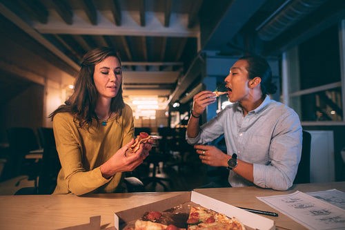 Business man and woman eating pizza late in the night at office