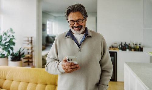 Senior man smiles at a mobile phone in his living room