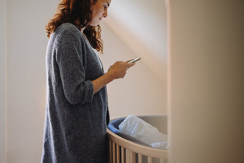 Woman standing by baby crib using mobile phone