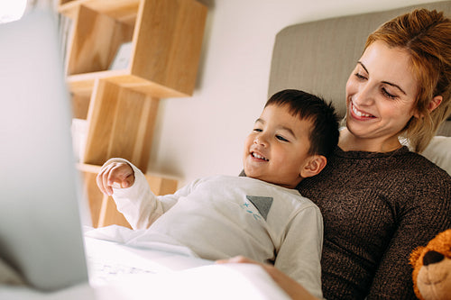 Happy mother and son using a laptop in bed