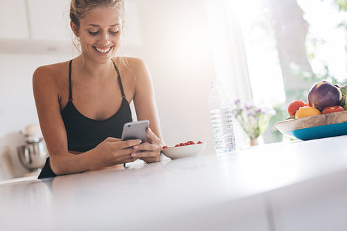 Smiling woman using smartphone in kitchen
