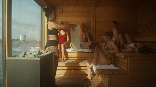 The group shares a sauna aufguss ritual as a woman directs heat through the spa