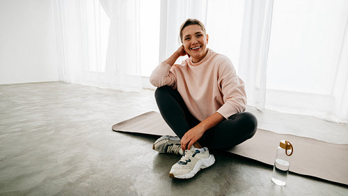 Recovery looks calm as the woman sits with water on her yoga mat indoors