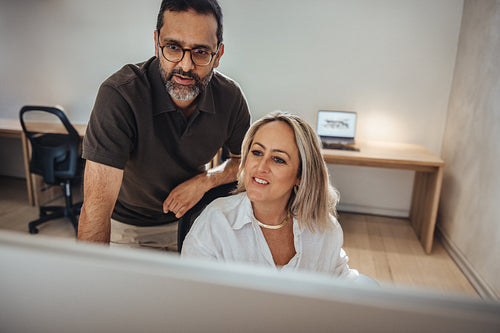 Middle-aged colleagues discuss a project on a computer in a modern office setting