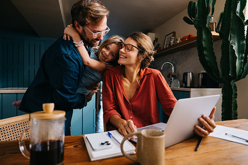 Brief family bonding moment as mom works on laptop at kitchen table