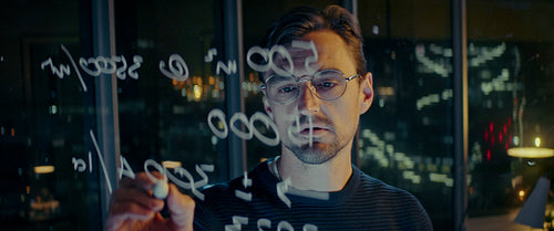 Businessman working late at night, solving equations on a glass board in his office