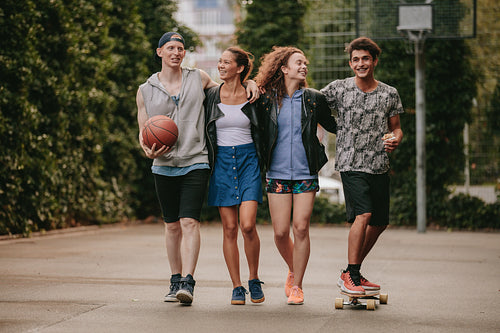 Young friends walking with skateboard and basketball