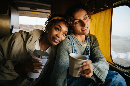 Two friends sit in a cozy van window seat sharing coffee and enjoying the journey together
