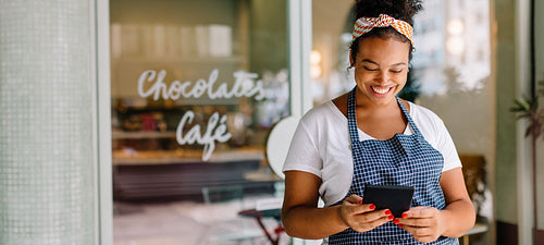 Happy female entrepreneur smiling with digital tablet and smartphone in her cafe