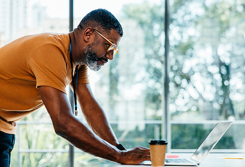 Focused businessman working on laptop in modern office with coffee and natural light