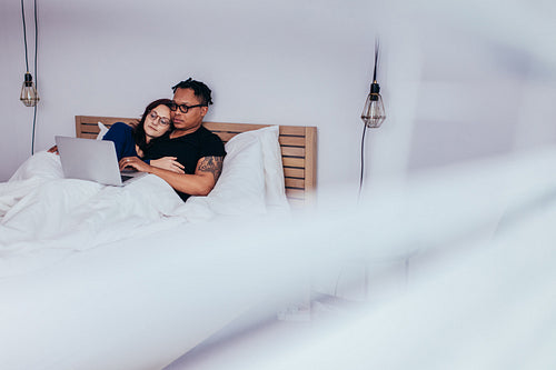 Multiracial couple relaxing in bedroom with laptop