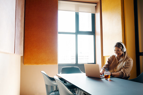 Woman wearing headphones working on a laptop in a modern office setting