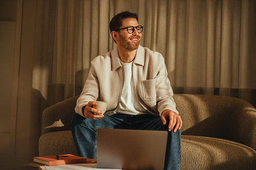 Happy businessman enjoys a coffee break with laptop on cozy couch