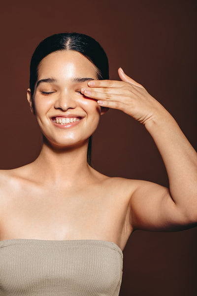 Enjoying the results of a female skincare routine: Young woman smiles as she touches her gorgeous and soft skin