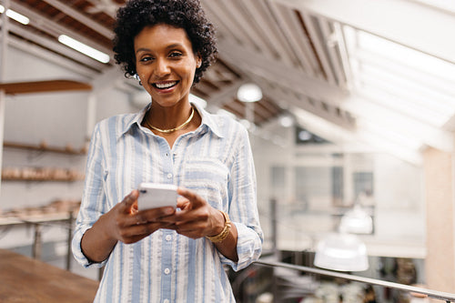 Cheerful small business owner using a smartphone in a warehouse