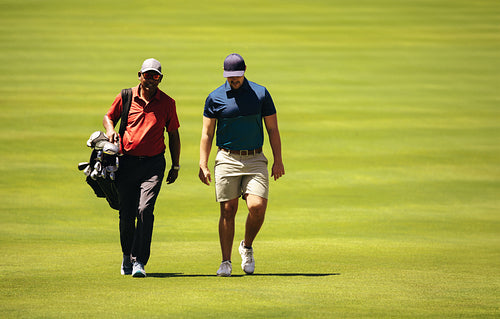 Caddy and golfer walking together on a sunny day, discussing strategy on the golf course during a competition