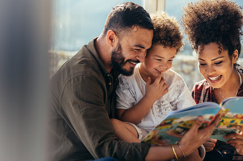 Smiling couple with kid reading a story book together