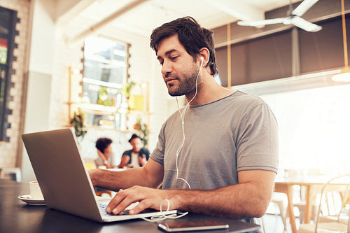 Young man with earphones using laptop at a cafe