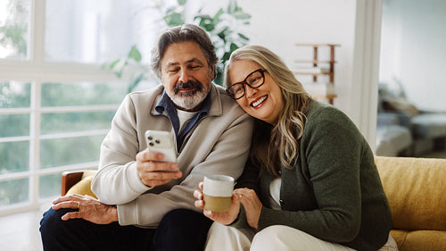 Glasses-wearing senior shares coffee and a smartphone at home