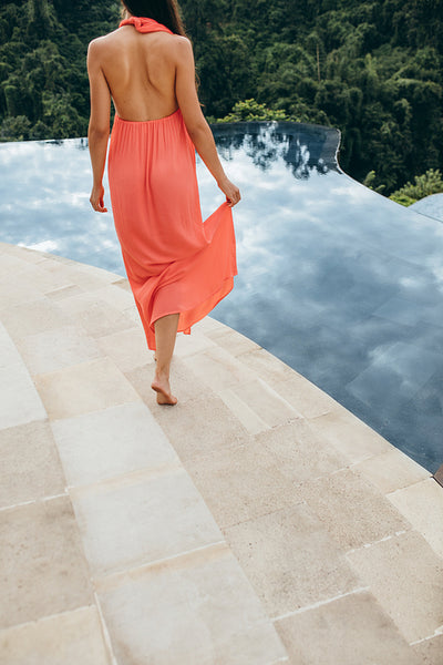 Woman in orange sundress walking along swimming pool