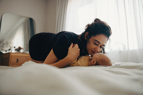 Mother kisses newborn on bed in tender moment