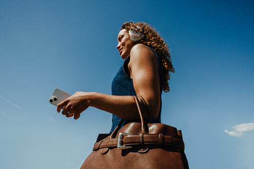 Focused businesswoman uses smartphone on commute against a blue sky