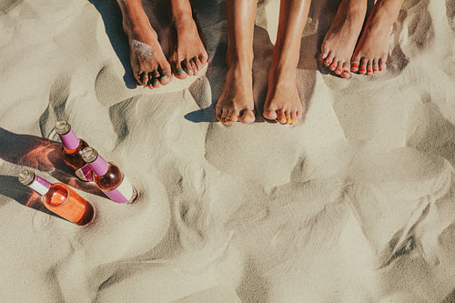 Close up of legs of three women beside bottles of soft drinks at the beach