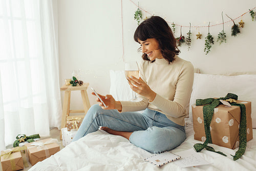 Woman enjoying wine sitting on bed and doing a video call