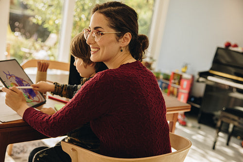 Woman sitting with son drawing on her digital tablet