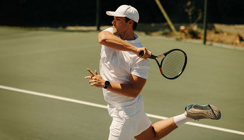Young man swinging tennis racket while jumping on court during a match