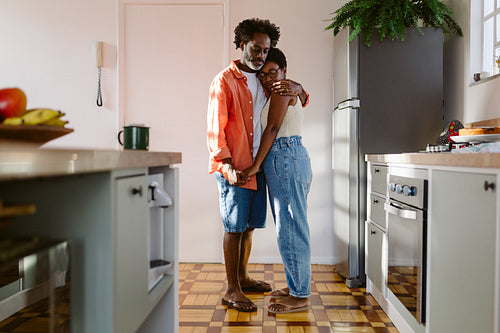 Loving husband holding his wife in his arms in their kitchen: A mature couple in love