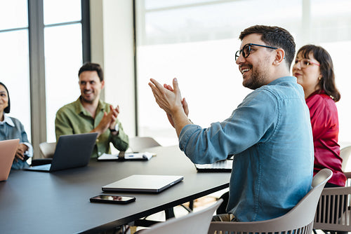 Colleagues engaged in a meeting and clapping in a bright office environment