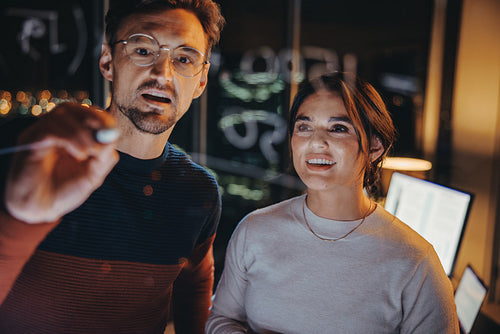 Late night strategy meeting: Two business people brainstorming on a glass wall