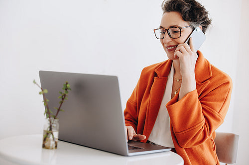 Mature businesswoman making a phone call and typing on a laptop while working in a cafe