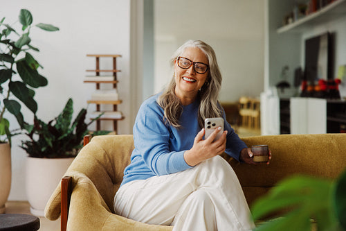 Glasses-wearing senior uses a phone in the living room