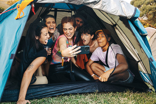 Happy young people taking fun selfies inside a festival camping tent